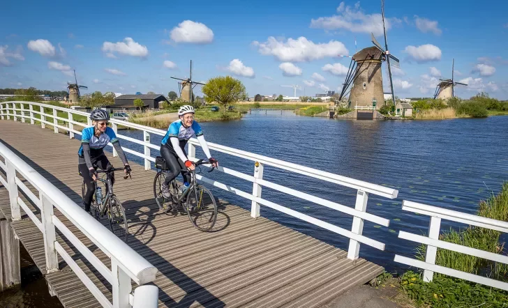 Bikers on small bridge with windmills in background