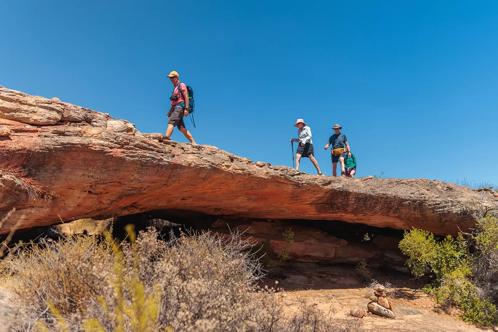 Three people hike over a rocky ledge