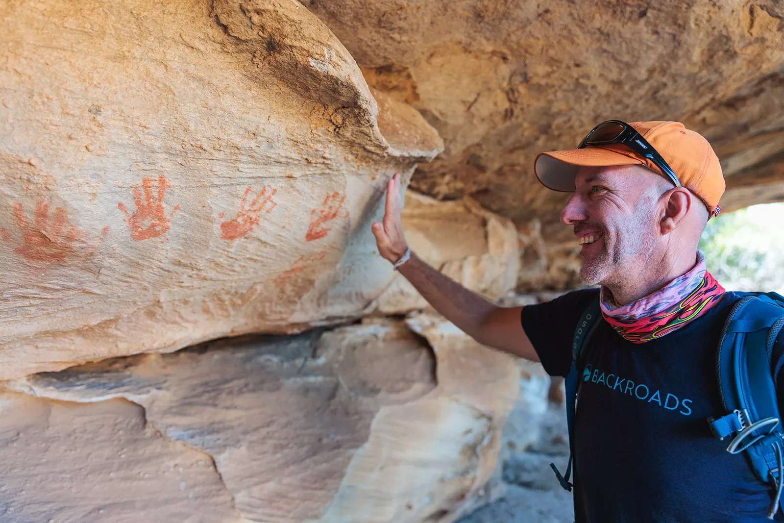 A man holds his hand up to handprints on a stone wall
