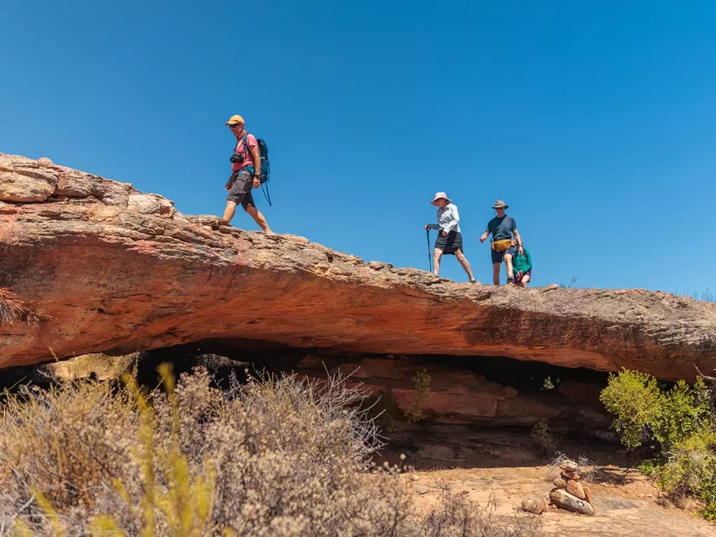 Three people hike over a rocky ledge 
