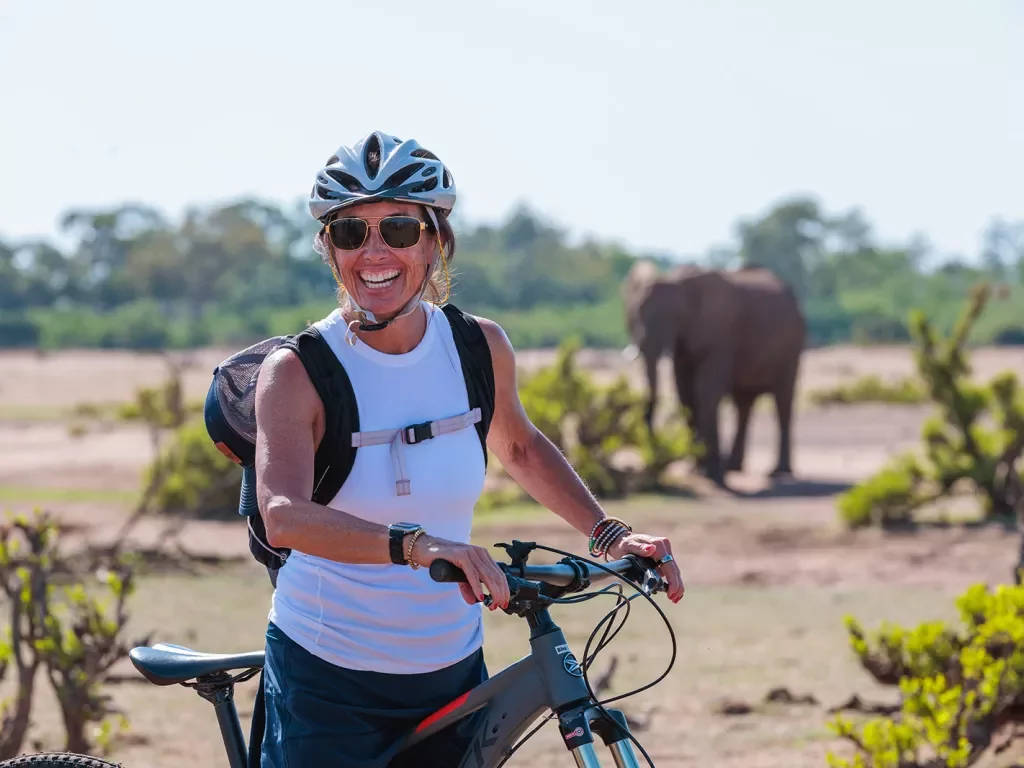 A person with a bike poses in front of an elephant