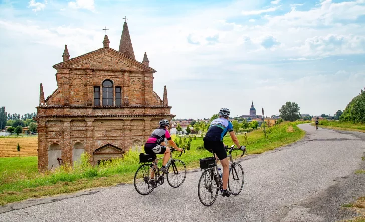 Cyclists riding along an Italian road with an old church building