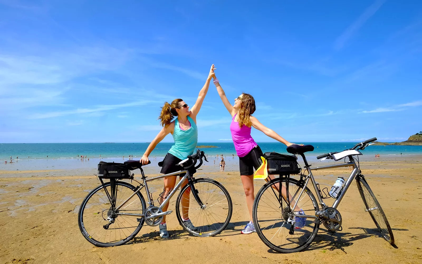Two Backroads Guests High Fiving on Beach with Bicycles