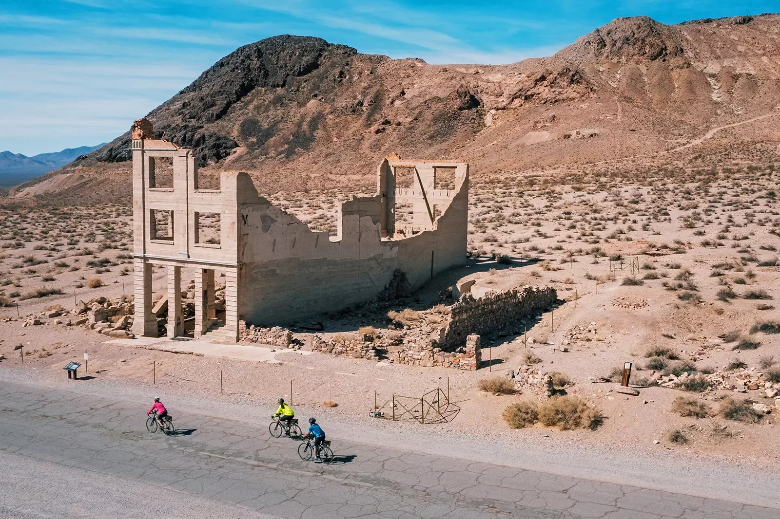 Guests biking through California desert with abandoned building in background.