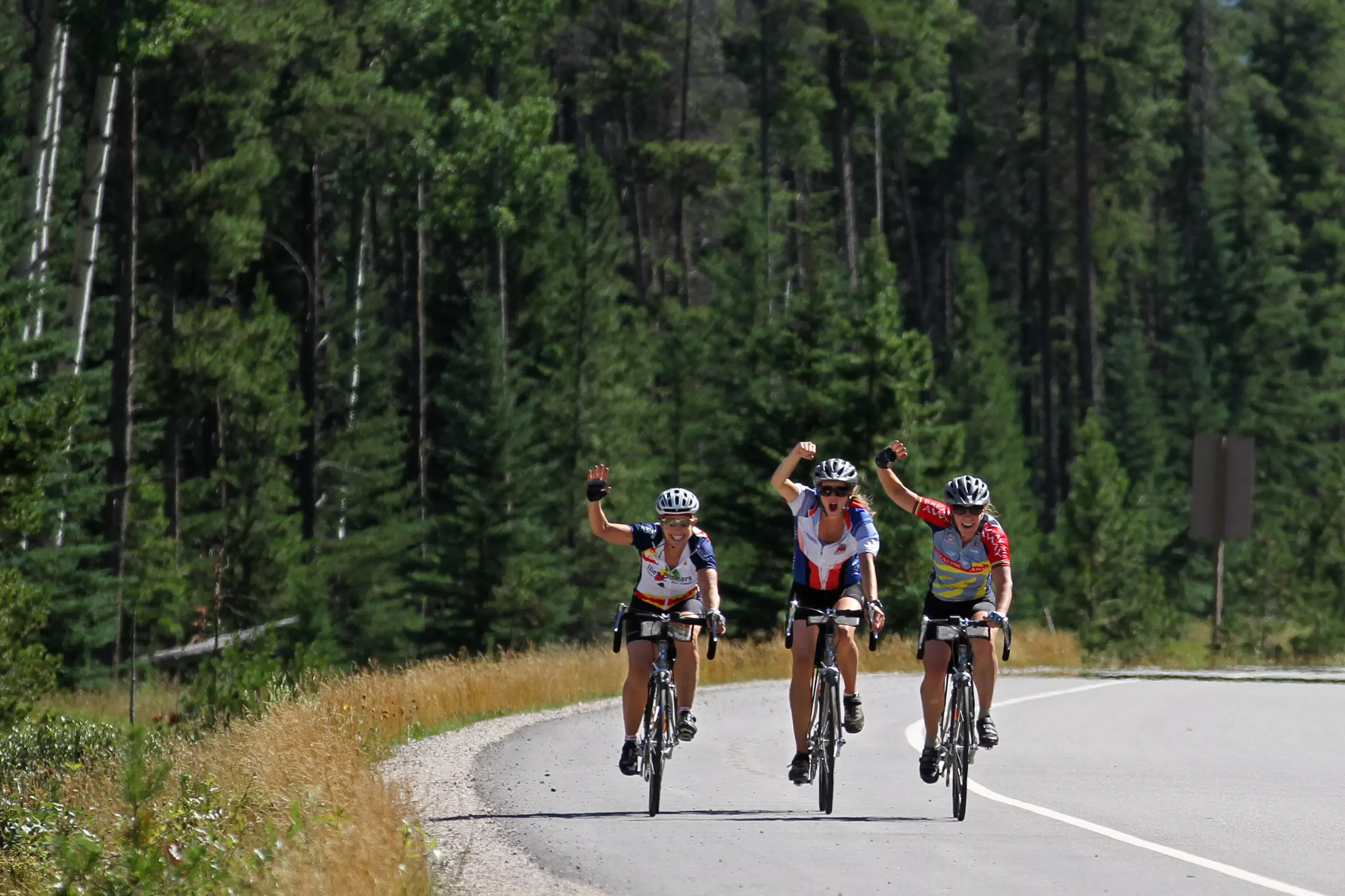 Three guests cycling down large road, waving at camera.