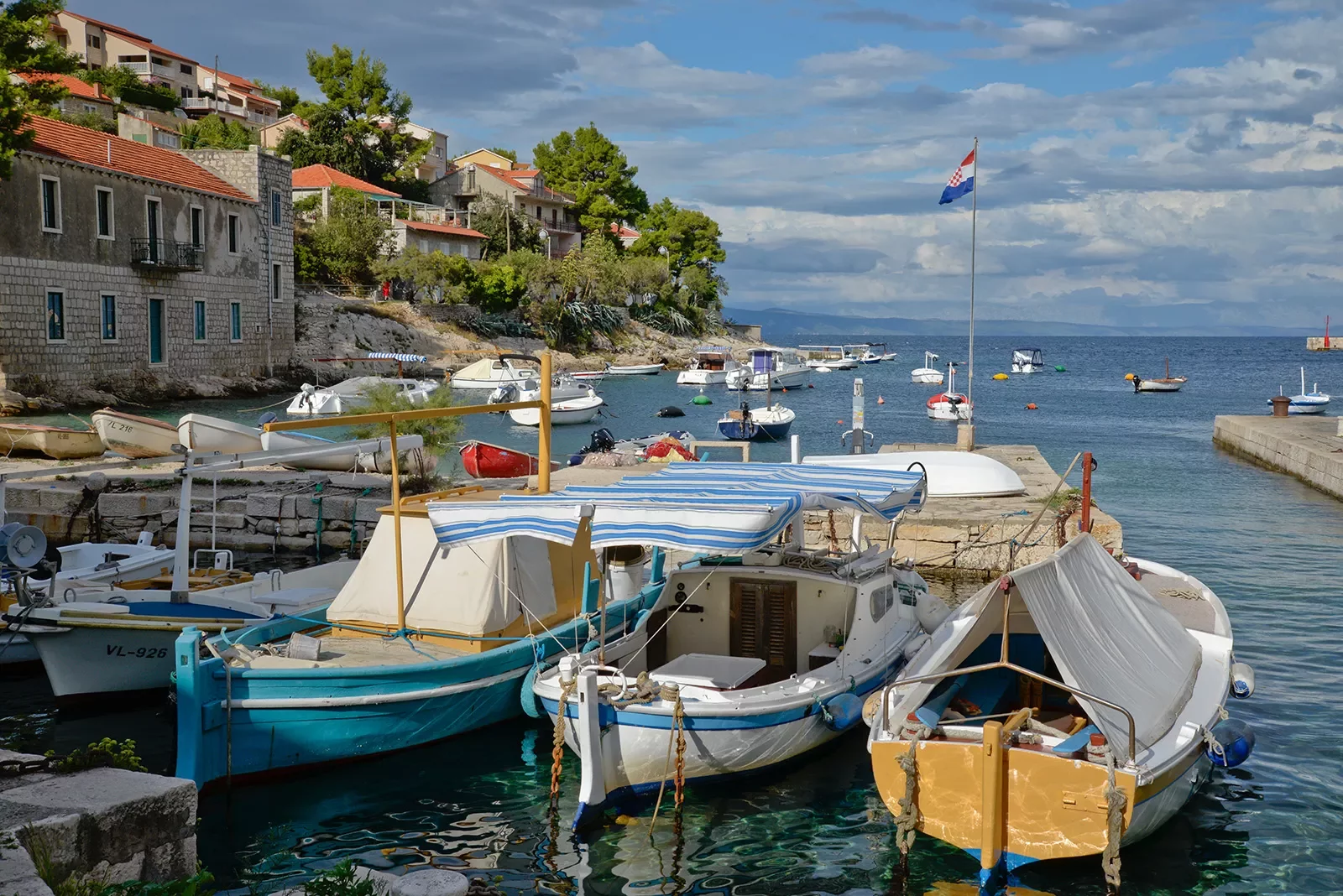 Wide shot of Croatian pier, numerous boats, coastal houses.