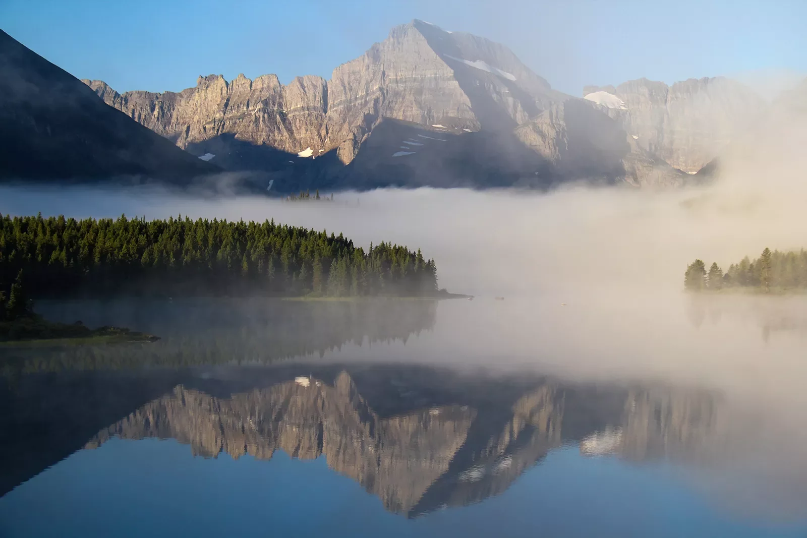 Fog wrapped around mountain in the background of reflective lake