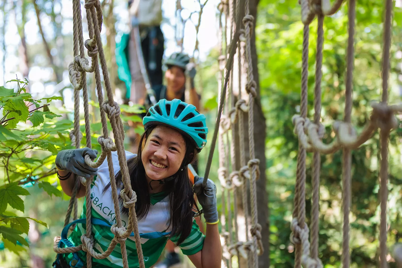 Young guest doing ropes course, smiling at camera.