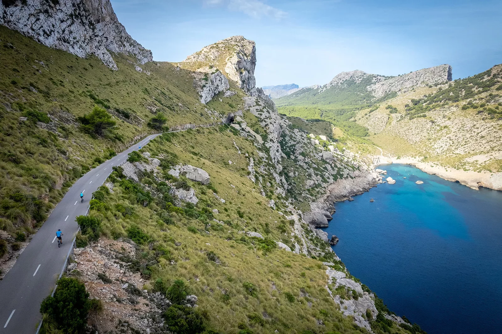 Two bikers riding around a bend on the coast of Mallorca.
