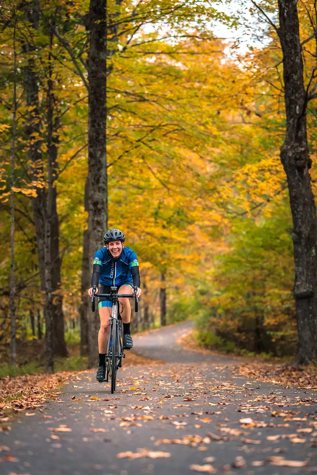 Guest cycling down autumnal road, smiling at camera.