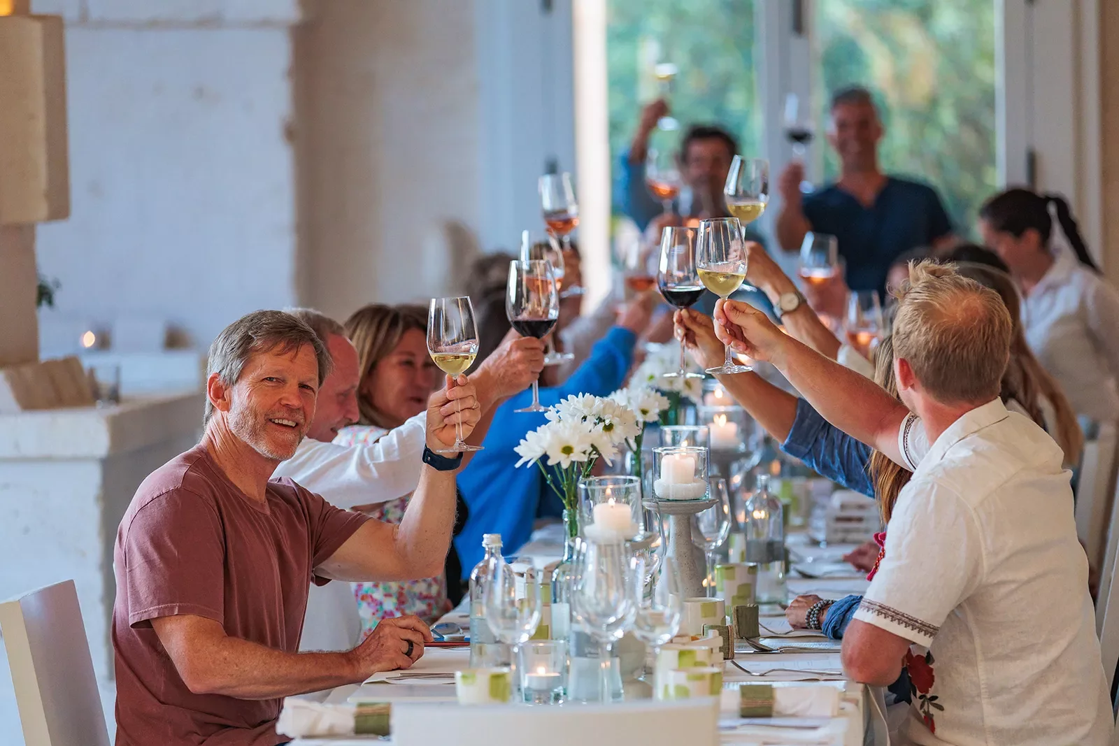 Group of guests at meal, toasting wine glasses.