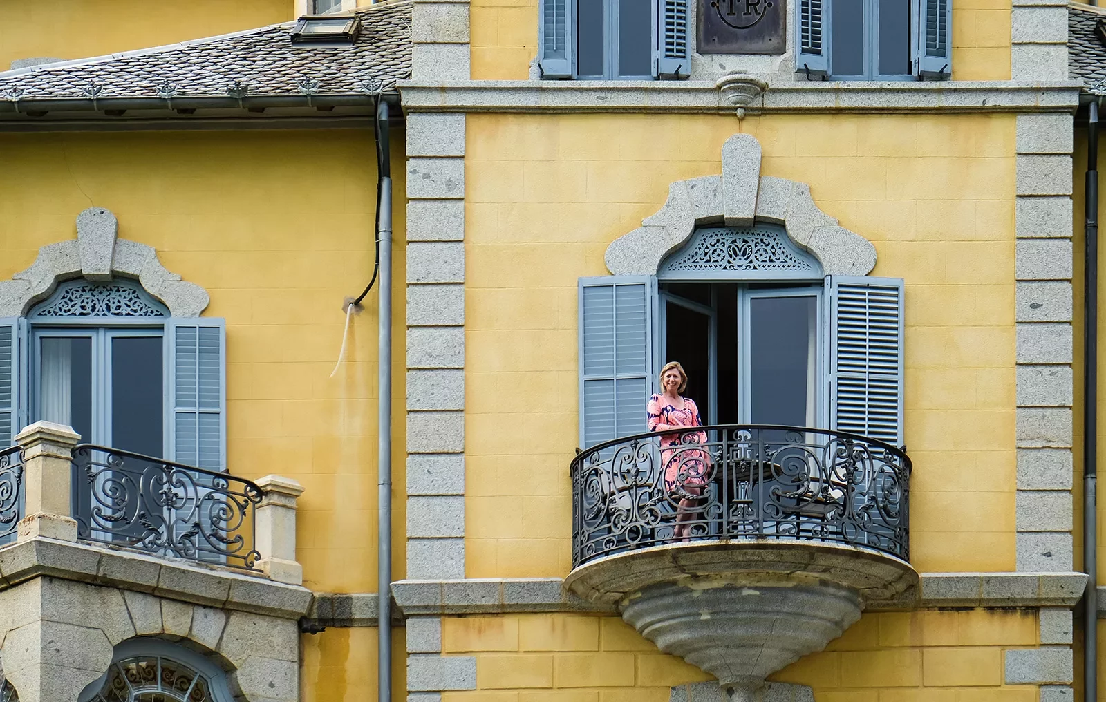 Woman standing on balcony of yellow building.