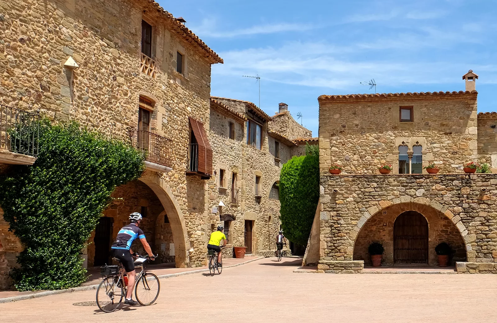 Two guests cycling through village, tan stone buildings all around.