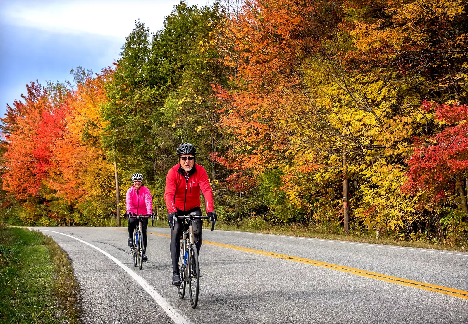 Two guests cycling down road, fall-colored trees to their left.