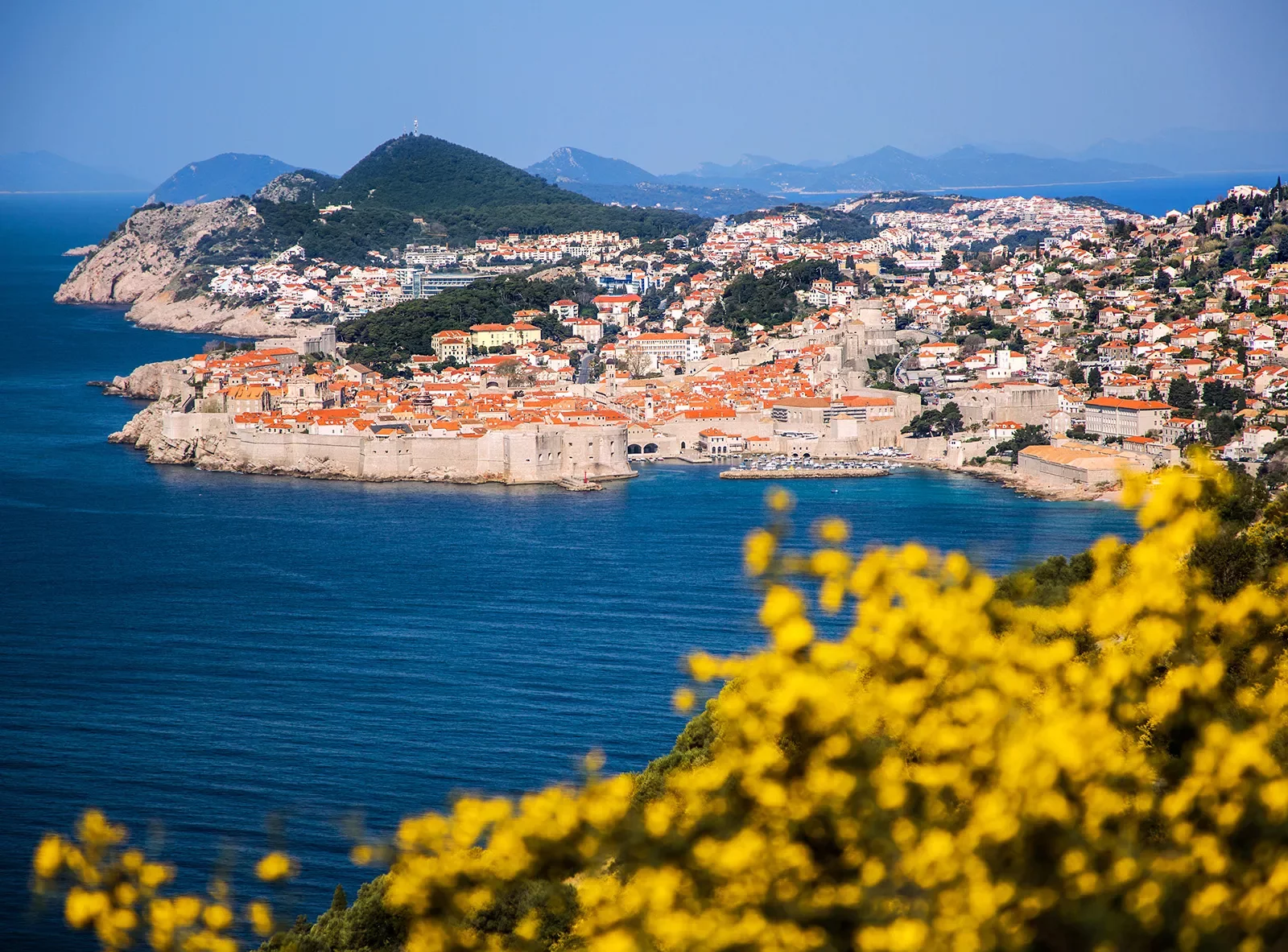 Wide shot of Dubrovnik coastline, blue ocean, white and tan houses.