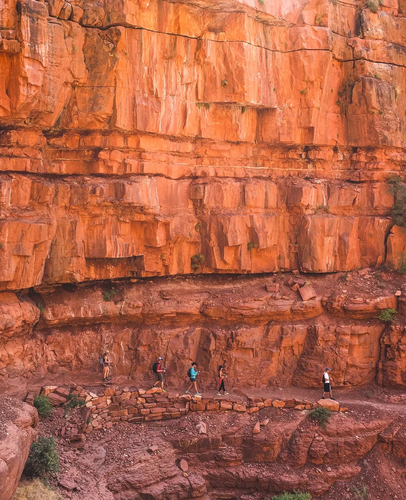 Five guests on cliffside trail, large orange rock face above them.