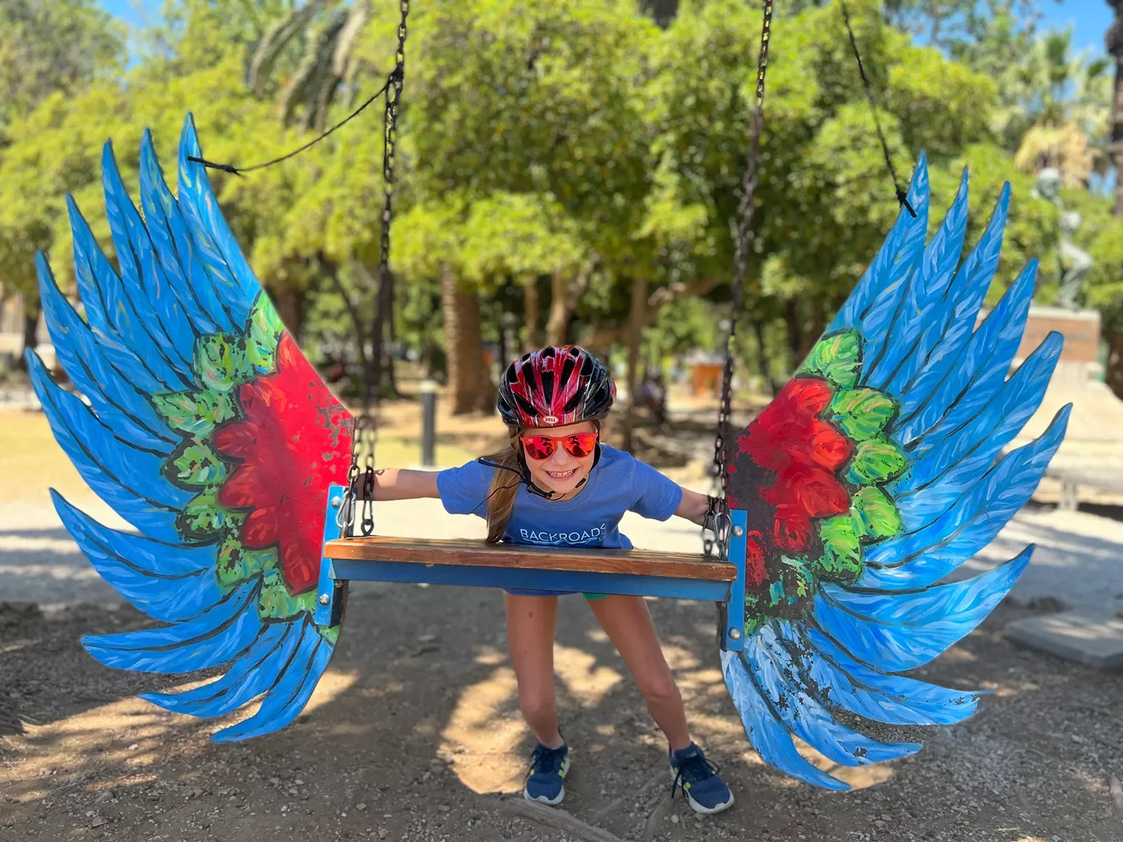 Young guest in bike gear on swing, colorful bird wings attached to it.