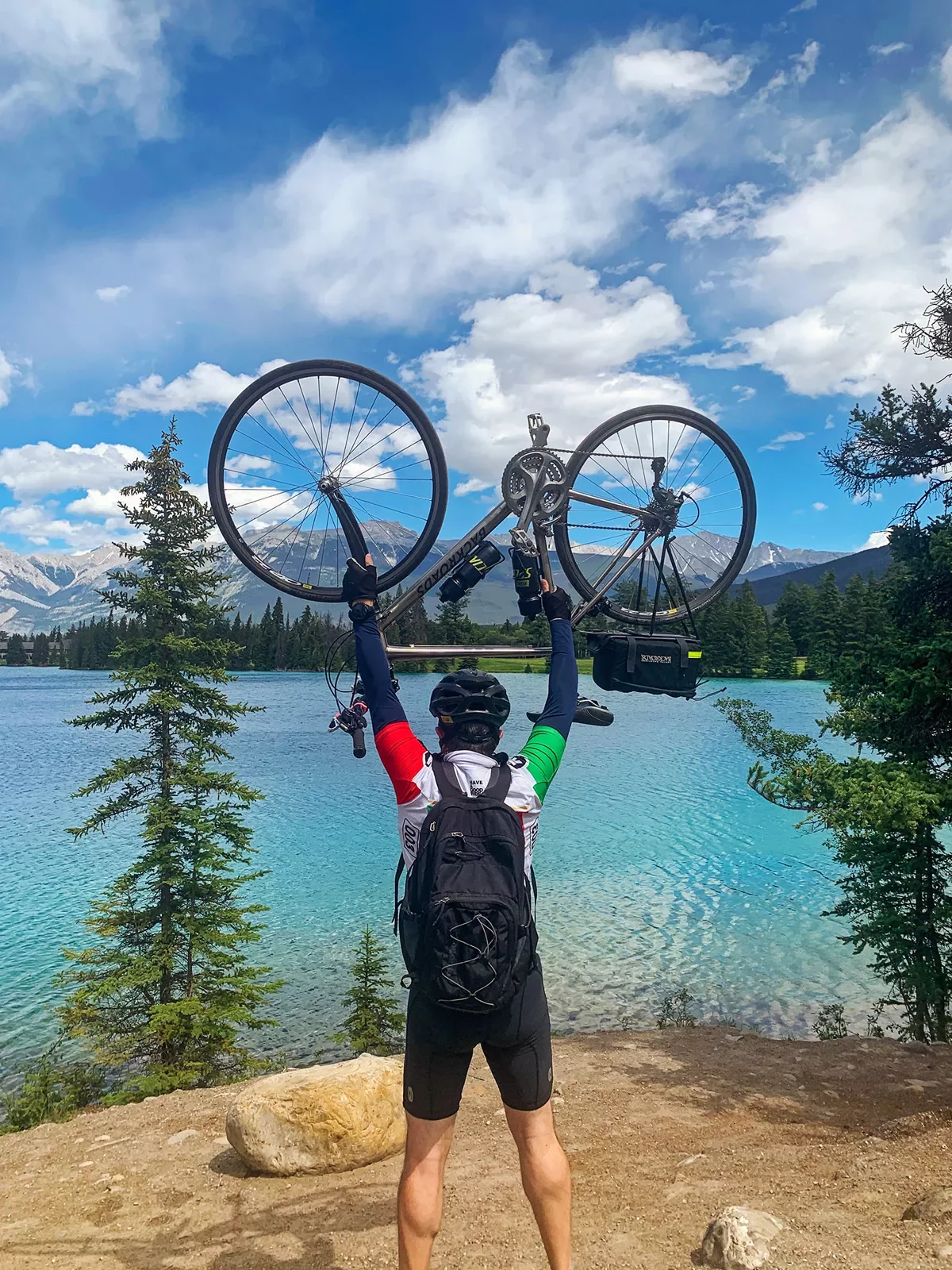 Guest holding bike over her head, lake, forest, hills in background.