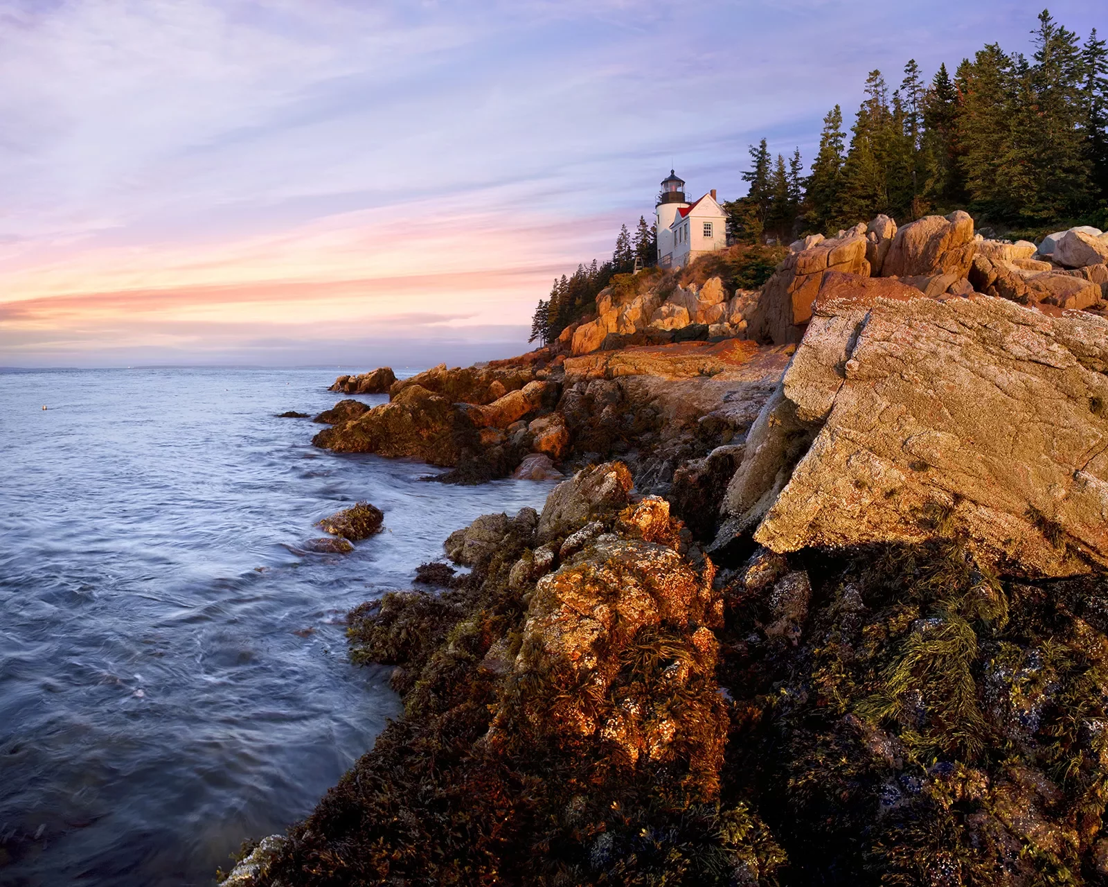 Wide shot of craggy inlet, small white lighthouse, sunset.