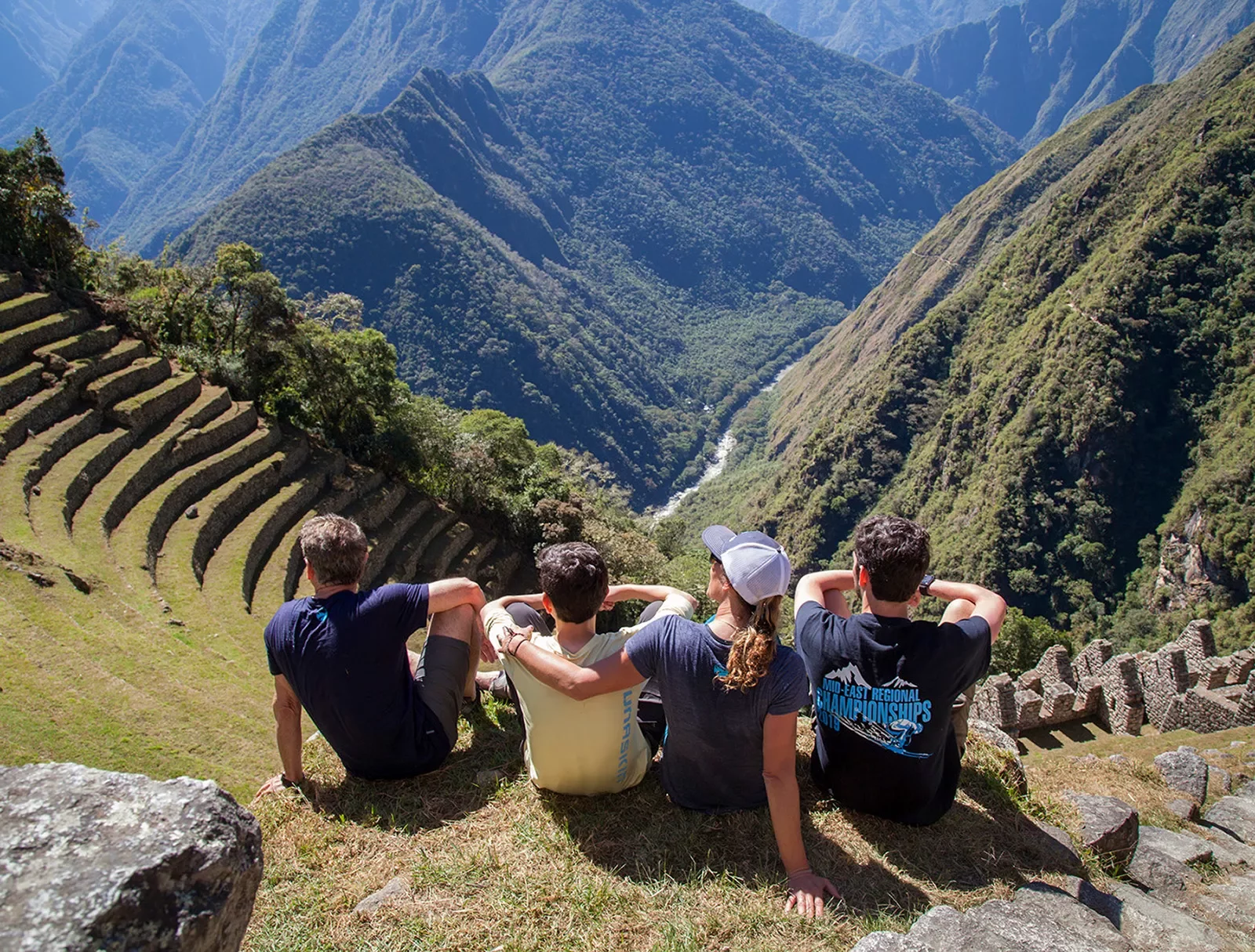 Four guests sitting on Machu Picchu hillside, overlooking mountains.