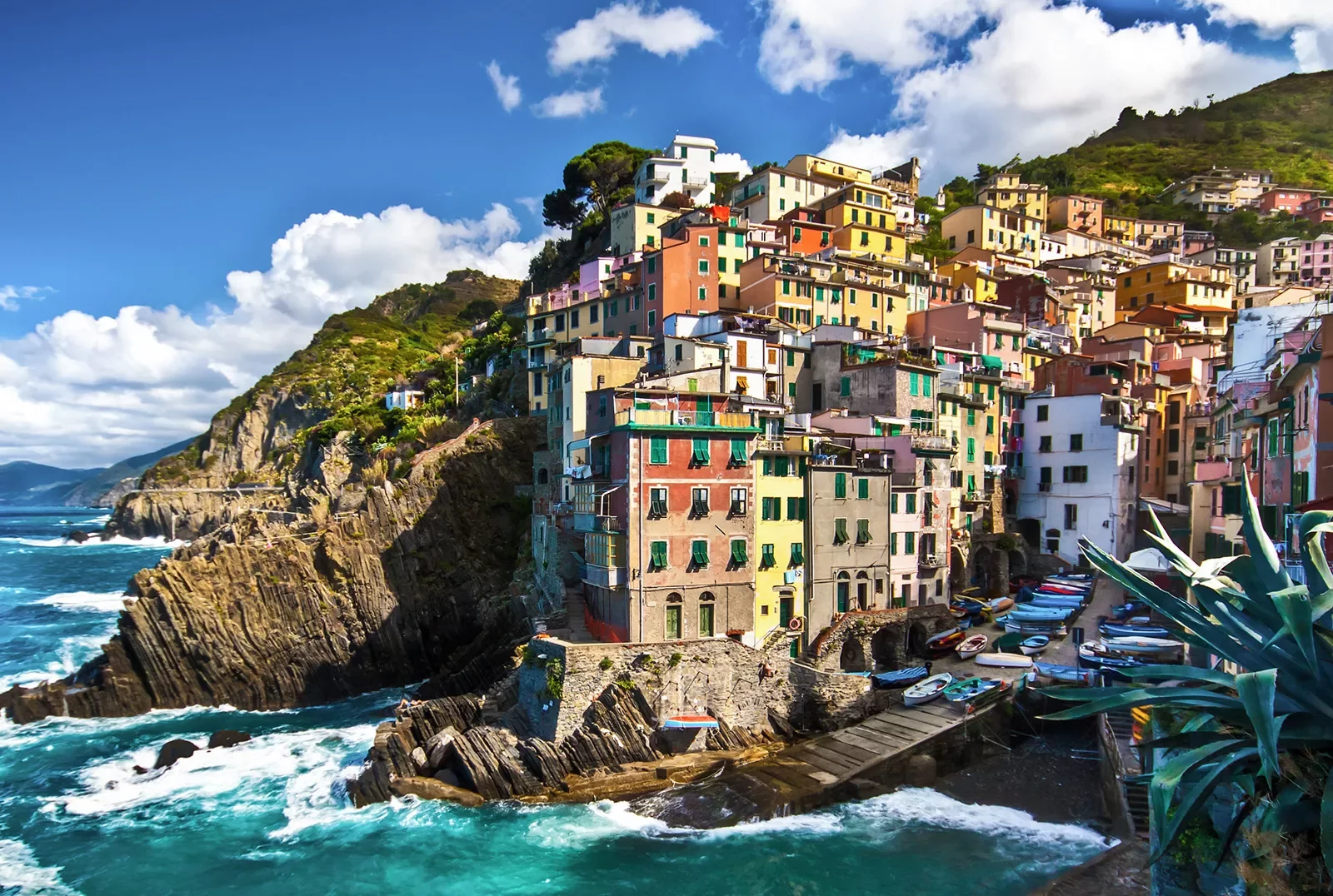 Wide shot of Cinque Terre houses, small pier and ocean down below.