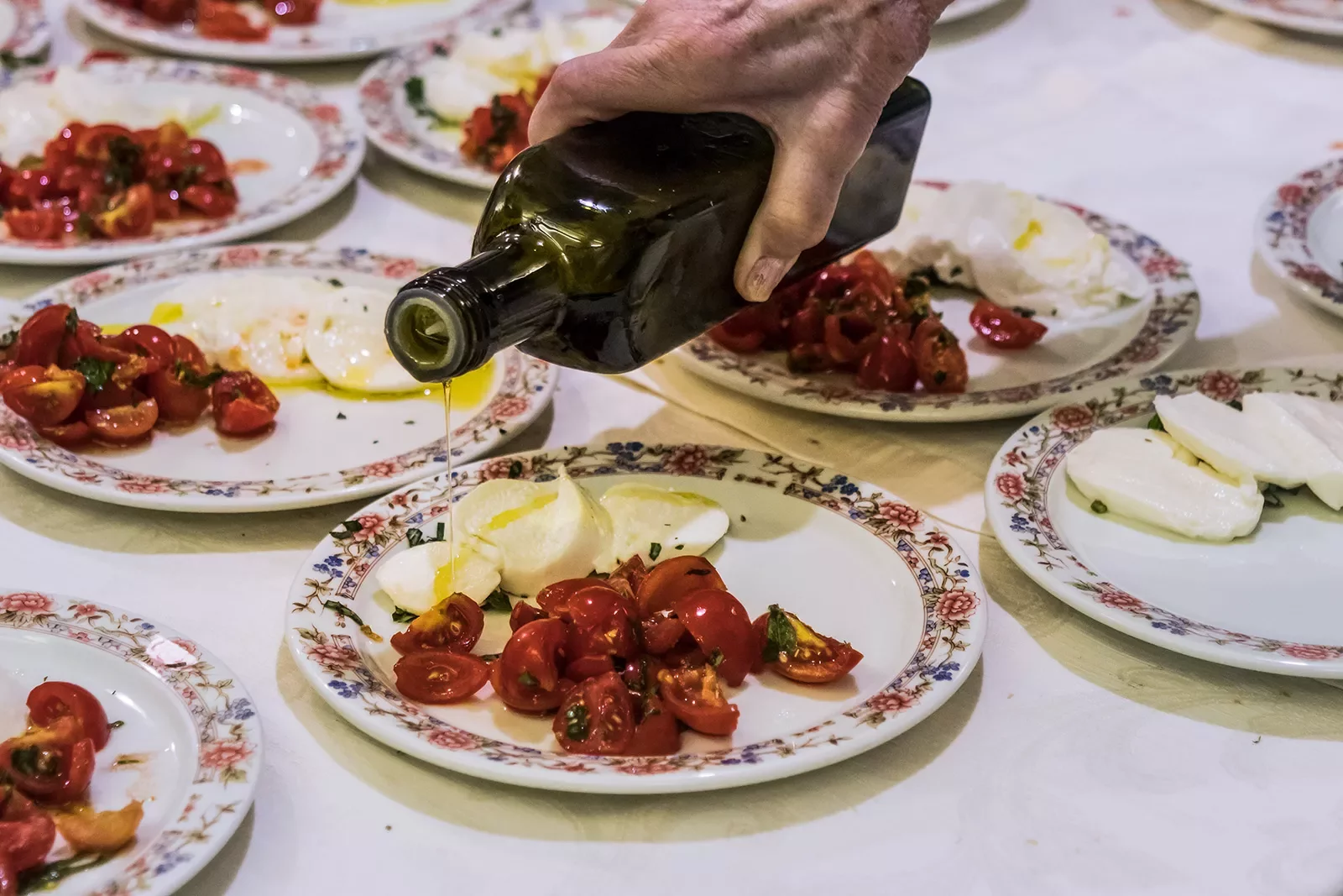 Plates of caprese salad, hand pouring olive oil.