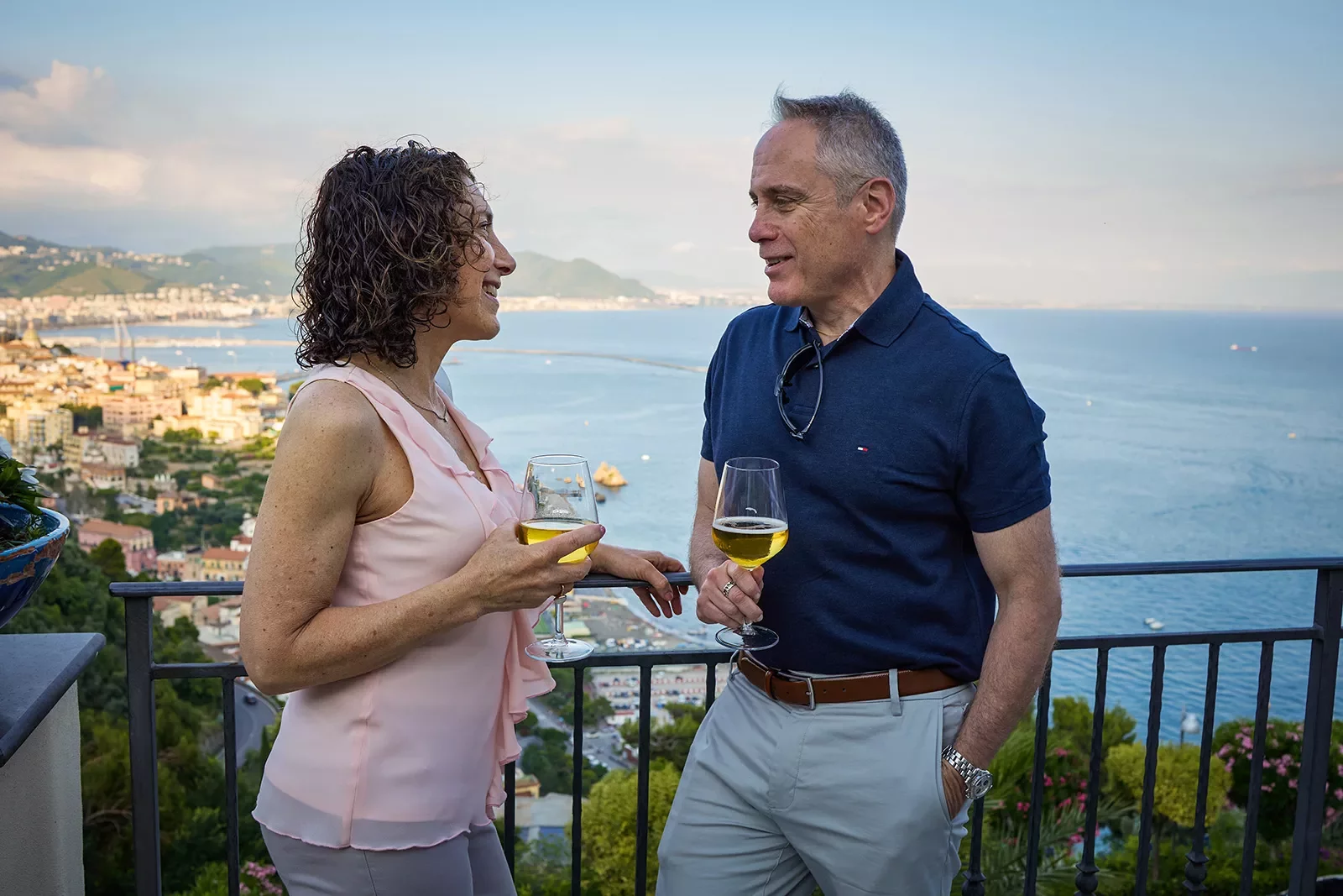 Two guests talking, wine glasses in hand, overlooking coastline.