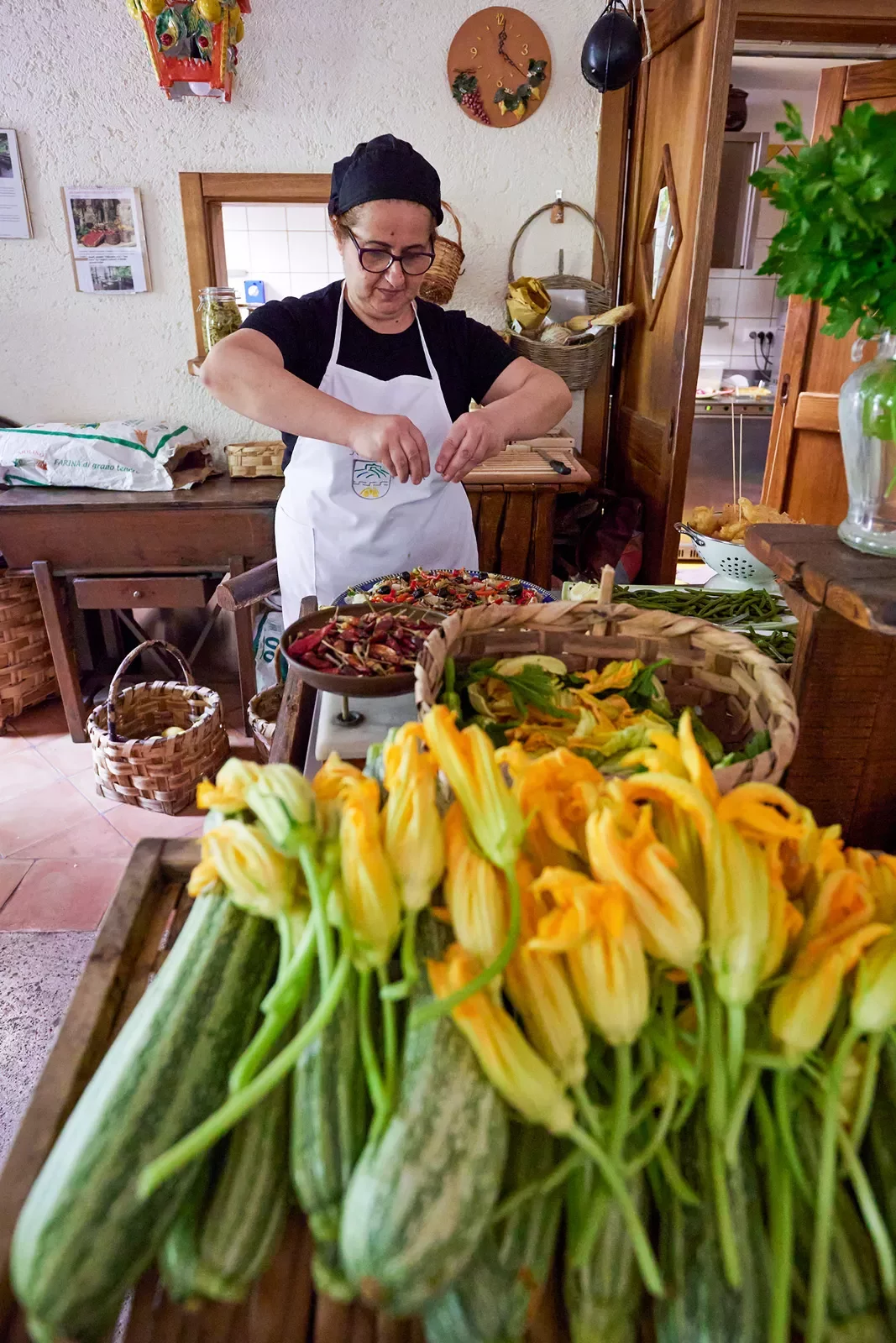 Local chef preparing food, zucchini + blossoms in foreground.