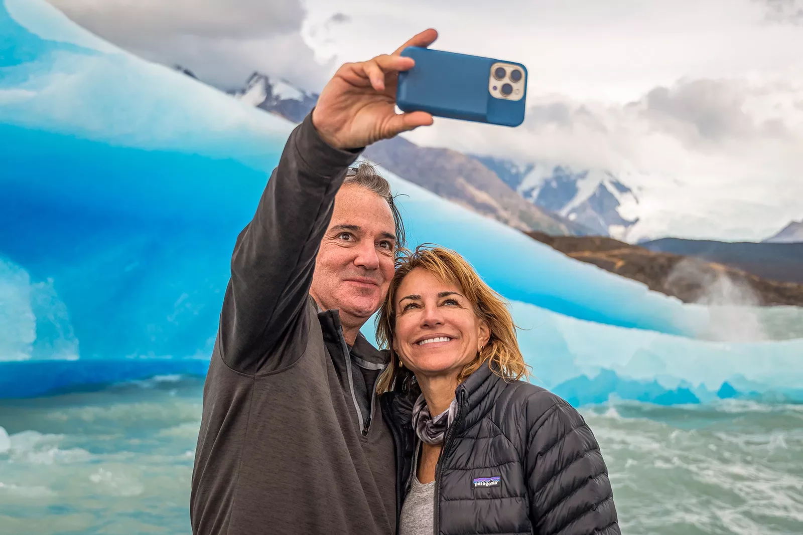 Two guests taking selfie in front of large glacier.