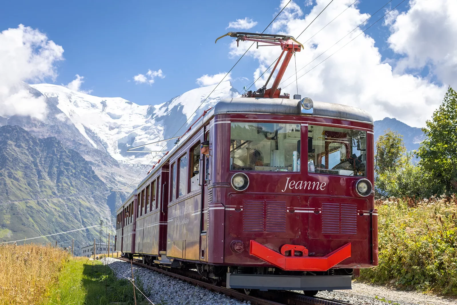 Shot of a red train, &quot;Jeanne&quot;, mountains &amp; clouds behind it.