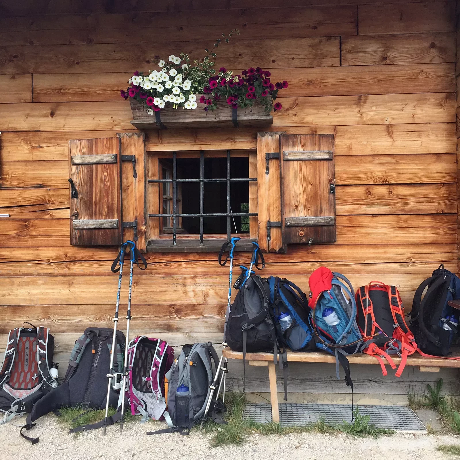 Hiking backpacks piled in front of log cabin.