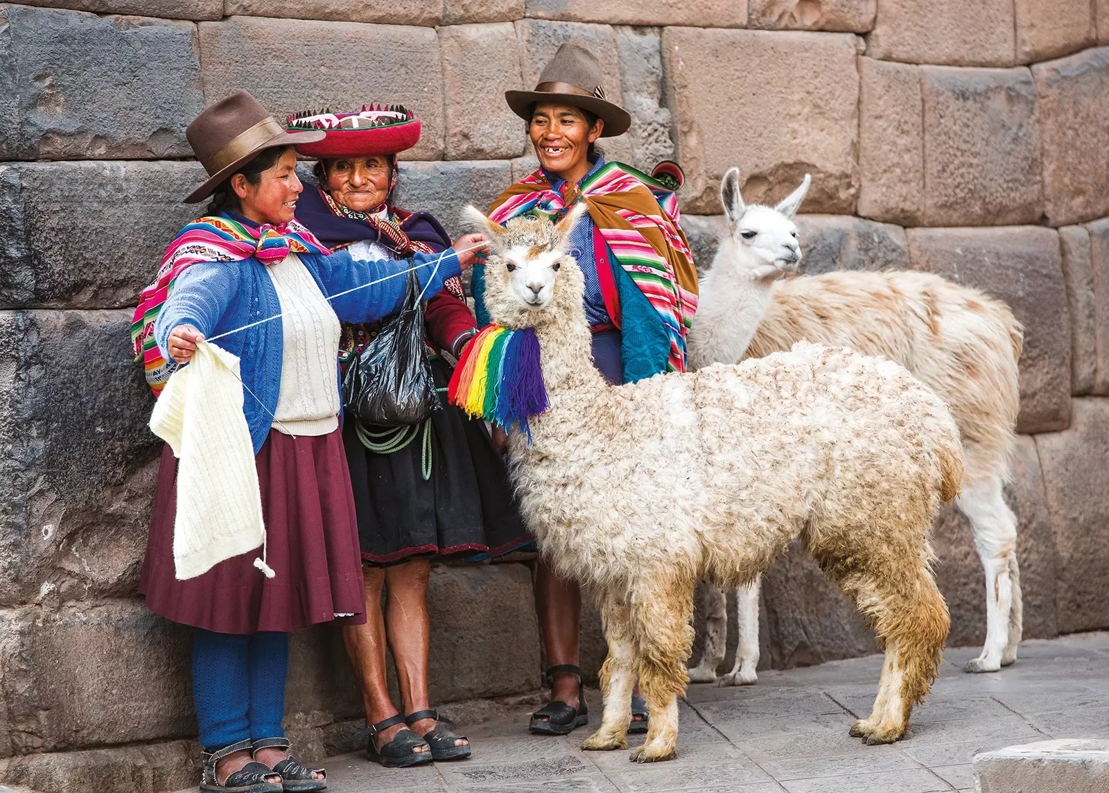 Three locals in colorful clothing, two llamas.