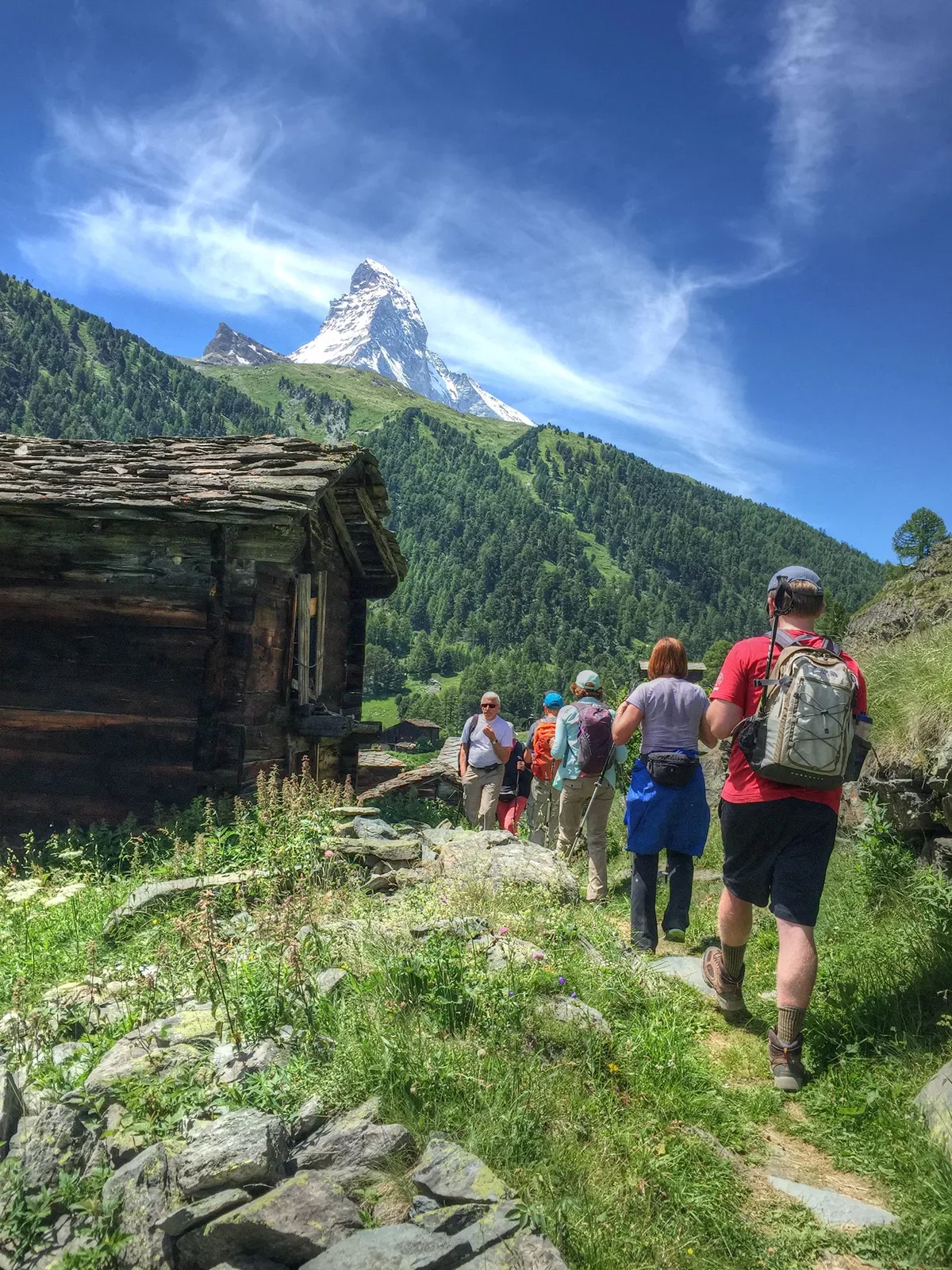 Group of guests walking past wooden shack, Matterhorn in distance.