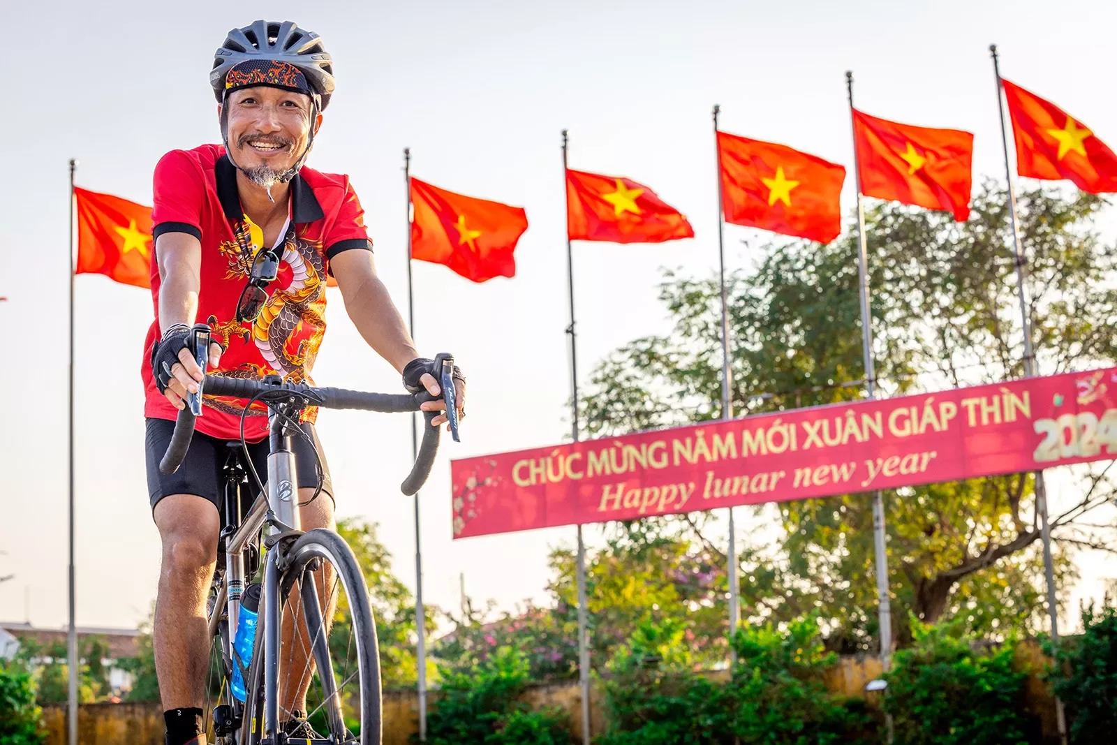 A man smiles while biking in front of a row of red flags