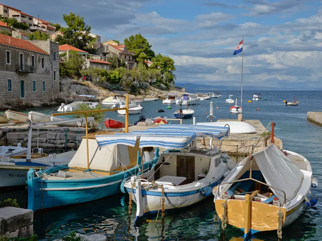 Wide shot of Croatian pier, numerous boats, coastal houses.