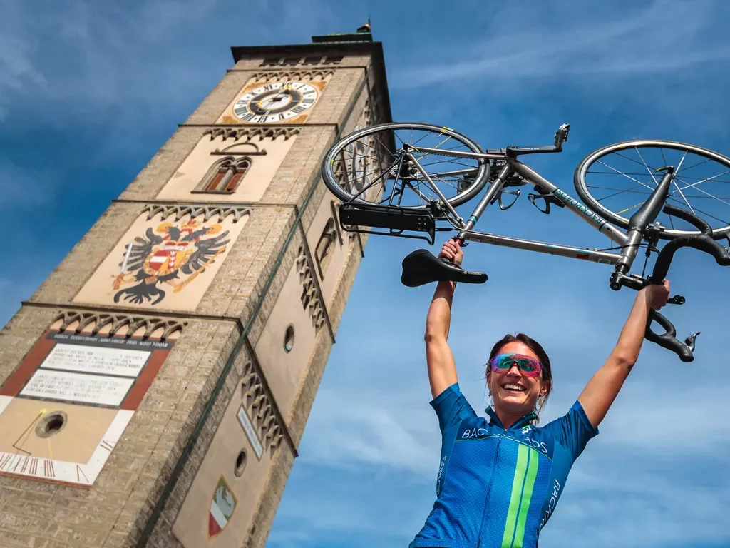 Biker holding a bike overhead with painted church tower in background. 