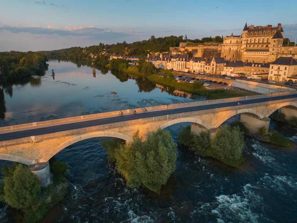 Bird's eye shot of cyclists over Loire River during sunset.  Château Royal d'Amboise behind.