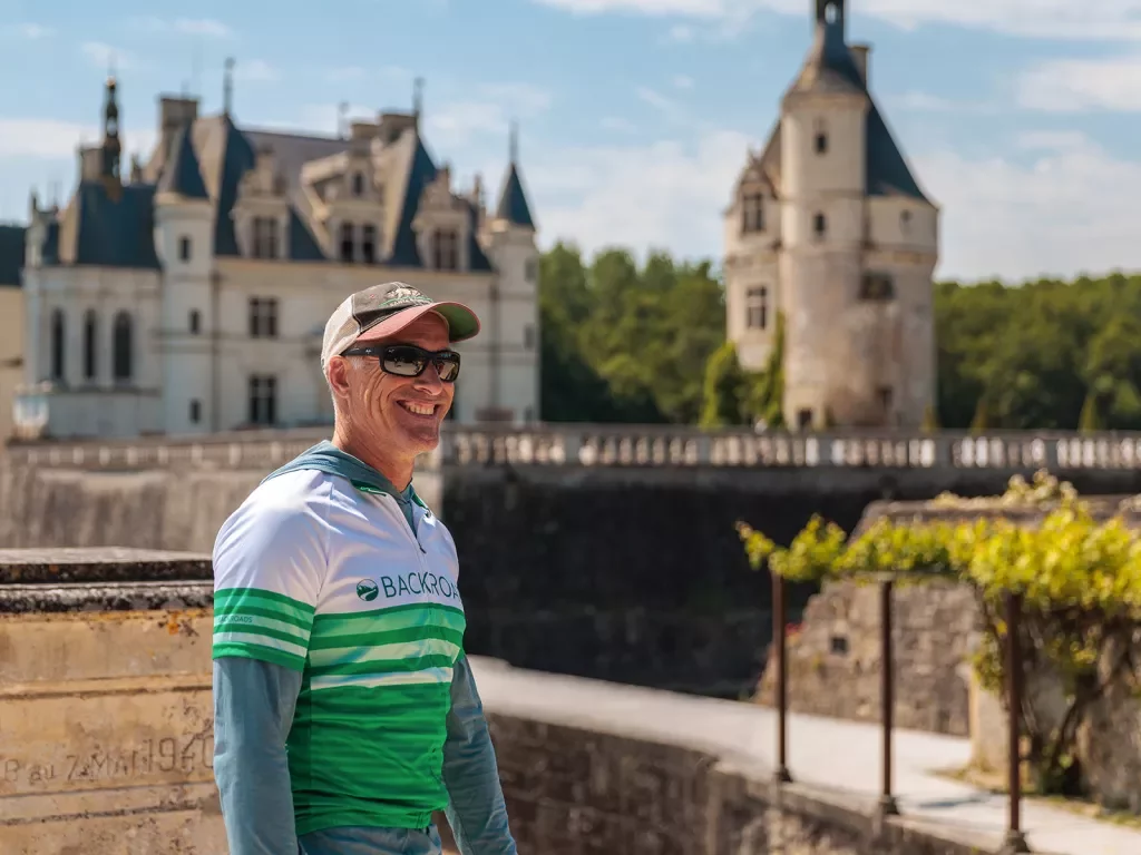 Guest smiling with green and white French chateau behind.
