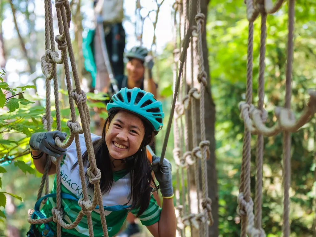 Young guest doing ropes course, smiling at camera.