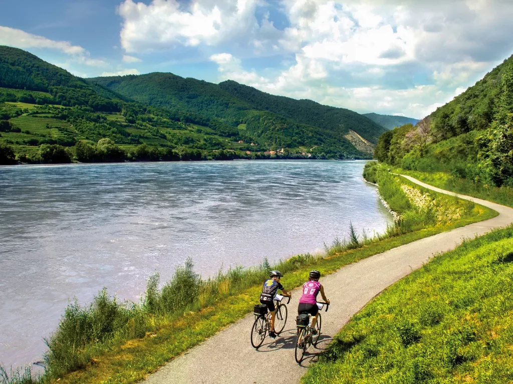 Two bikers riding on road alongside Danube River.
