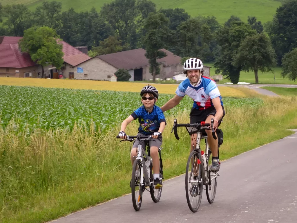 Child being helped on bike ride by adult.