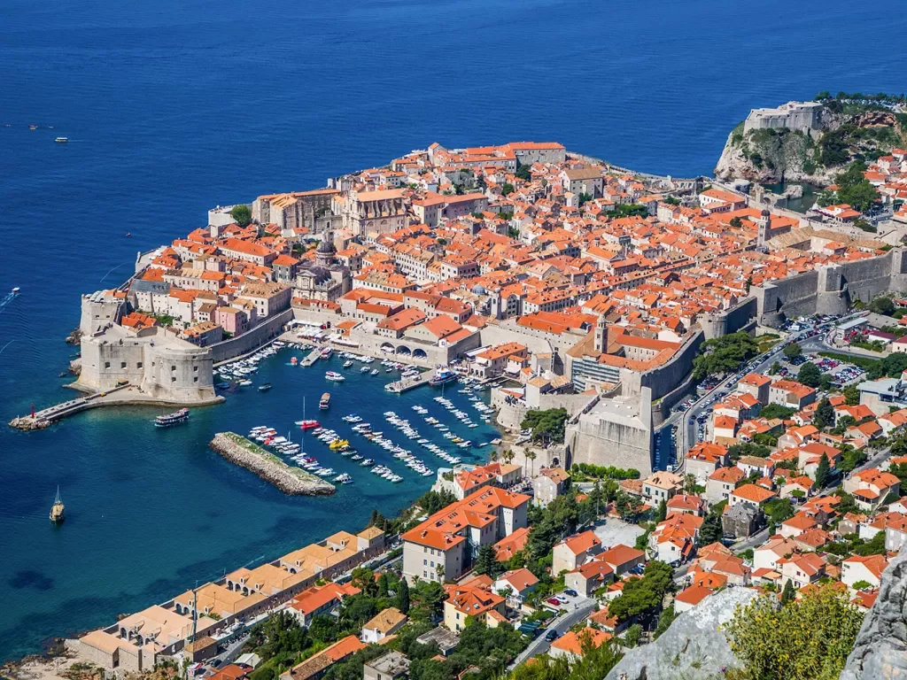 Bird's eye shot of Dubrovnik coastline, walled city, small boats, etc.