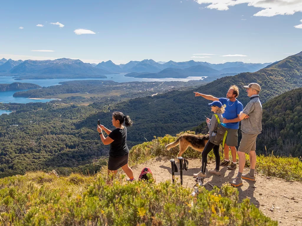 Four guests and dog on mountaintop, overlooking rivers, streams, forests, other mountains.