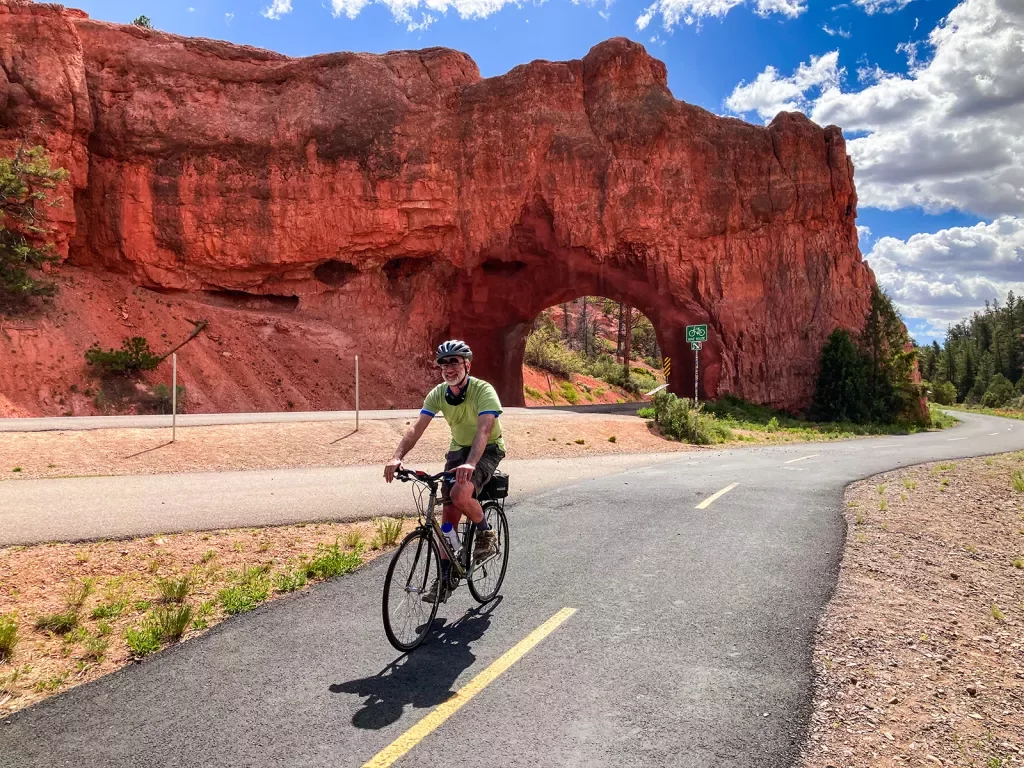 Guest cycling down street, large, orange rock archway behind him.