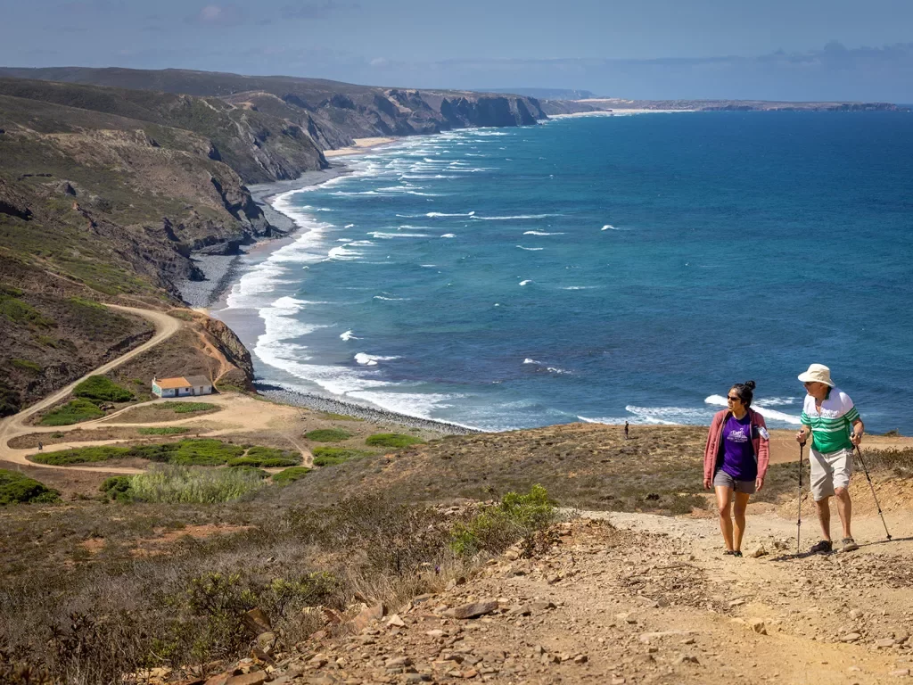 Two hikers walking up a sandy hill with the ocean in the background