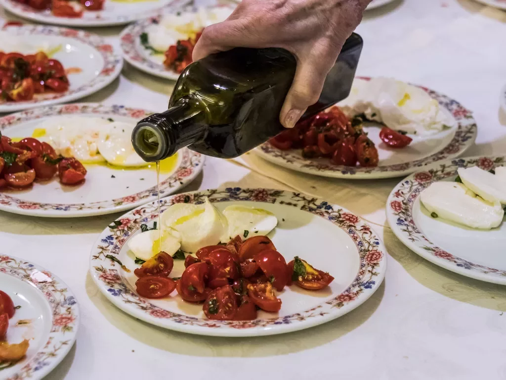 Plates of caprese salad, hand pouring olive oil.