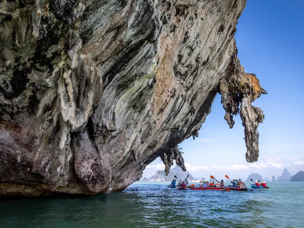 Kayakers paddling under stone cliffs