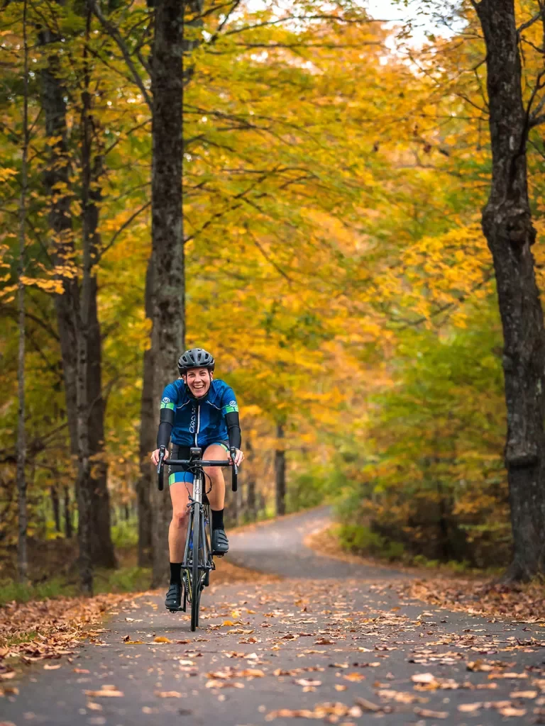 Guest cycling down autumnal road, smiling at camera.