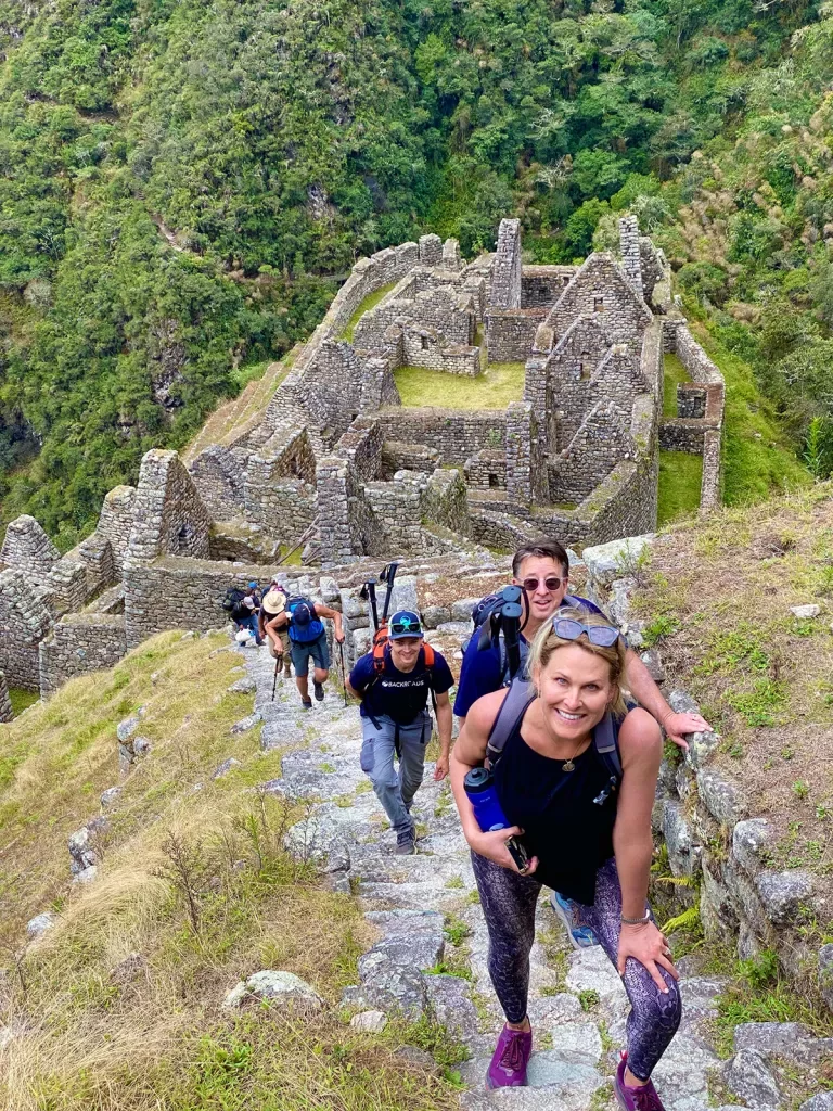 Guests hiking up stone trail, Machu Picchu ruins behind them.
