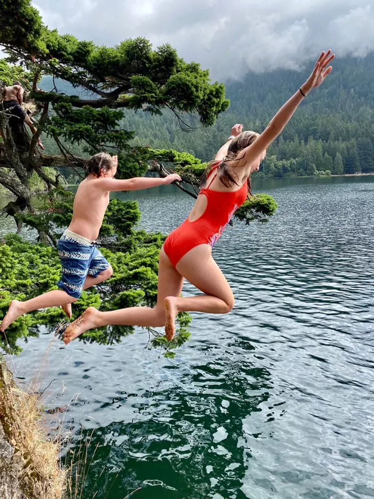 Two young guests jumping into ocean, fog, hills behind them.